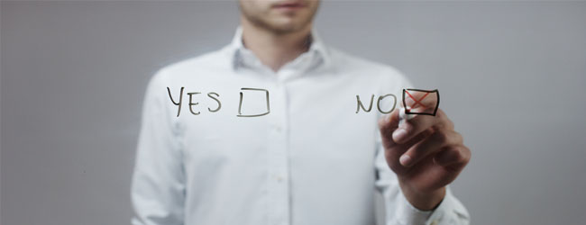 A person pointing at two written options, “Yes” and “No,” on a transparent surface and marking the “No” box with an X, indicating a decision or rejection.