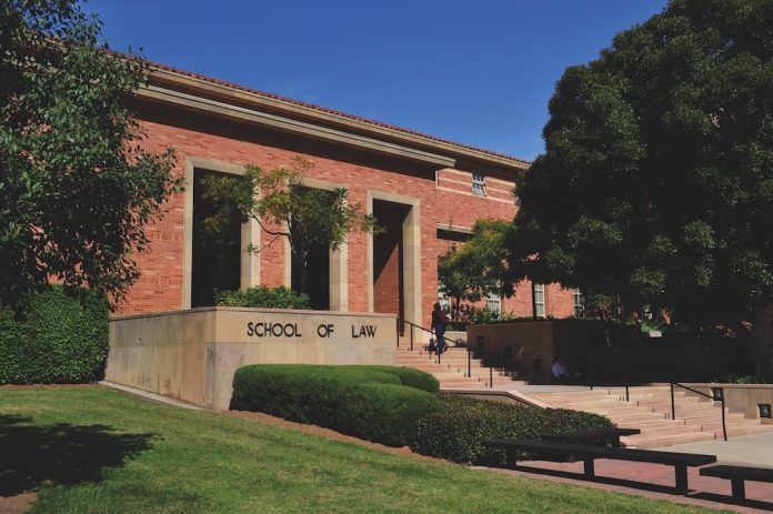UCLA School of Law building with red brick walls and “SCHOOL OF LAW” engraved on a stone sign beside the entrance steps.